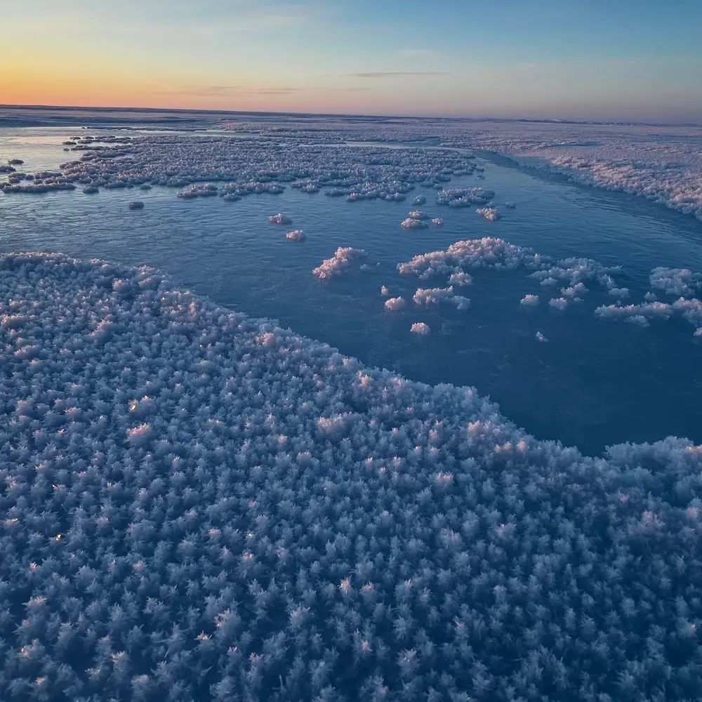 Photo of water on an ice plain freezing with a sunset in the background