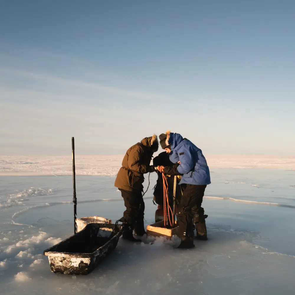 Photo of a team of people dressed in warm winter gear working on a water pump on an ice plain