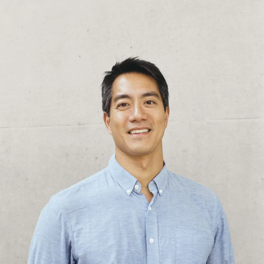 A photo of Mike Tsang smiling against a grey background.