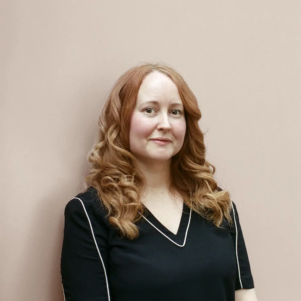 A photo of Cat Townley smiling and standing against a cream background.